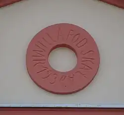 Godło domu umieszczone na szczycie elewacji frontowej - kółko z wpisanym w nie tekstem: „Willa Pod Skałą r 1934”, tzn. oryginalna, przedwojenna nazwa willi i rok ukończenia budowy.